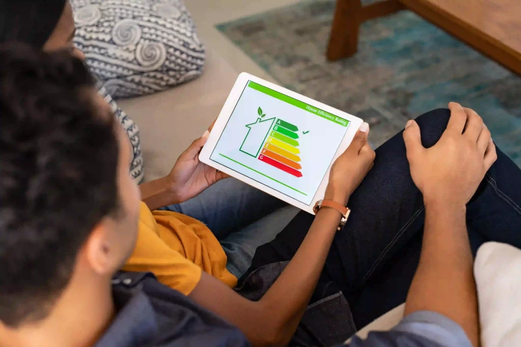Two people sit with a tablet showing an A-G energy efficiency chart, discussing eco-friendly choices at home.