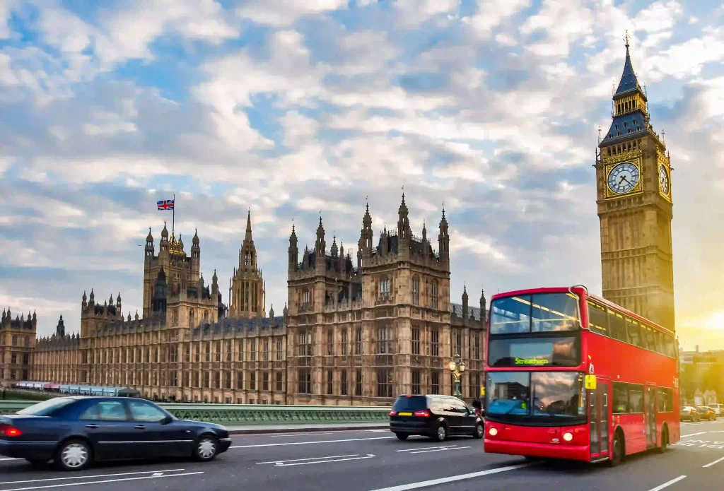 London's Big Ben and Parliament with a red double-decker bus, cars, and a cloudy sky backdrop.